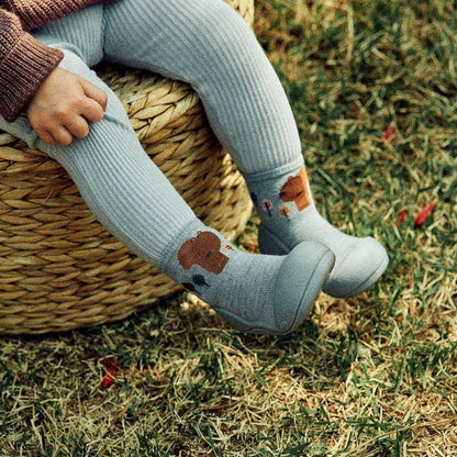 Pequena criança a usar meias cinzentas com padrão de esquilo e sapatos Attipas Woodland Blue Squirrel em ambiente natural.