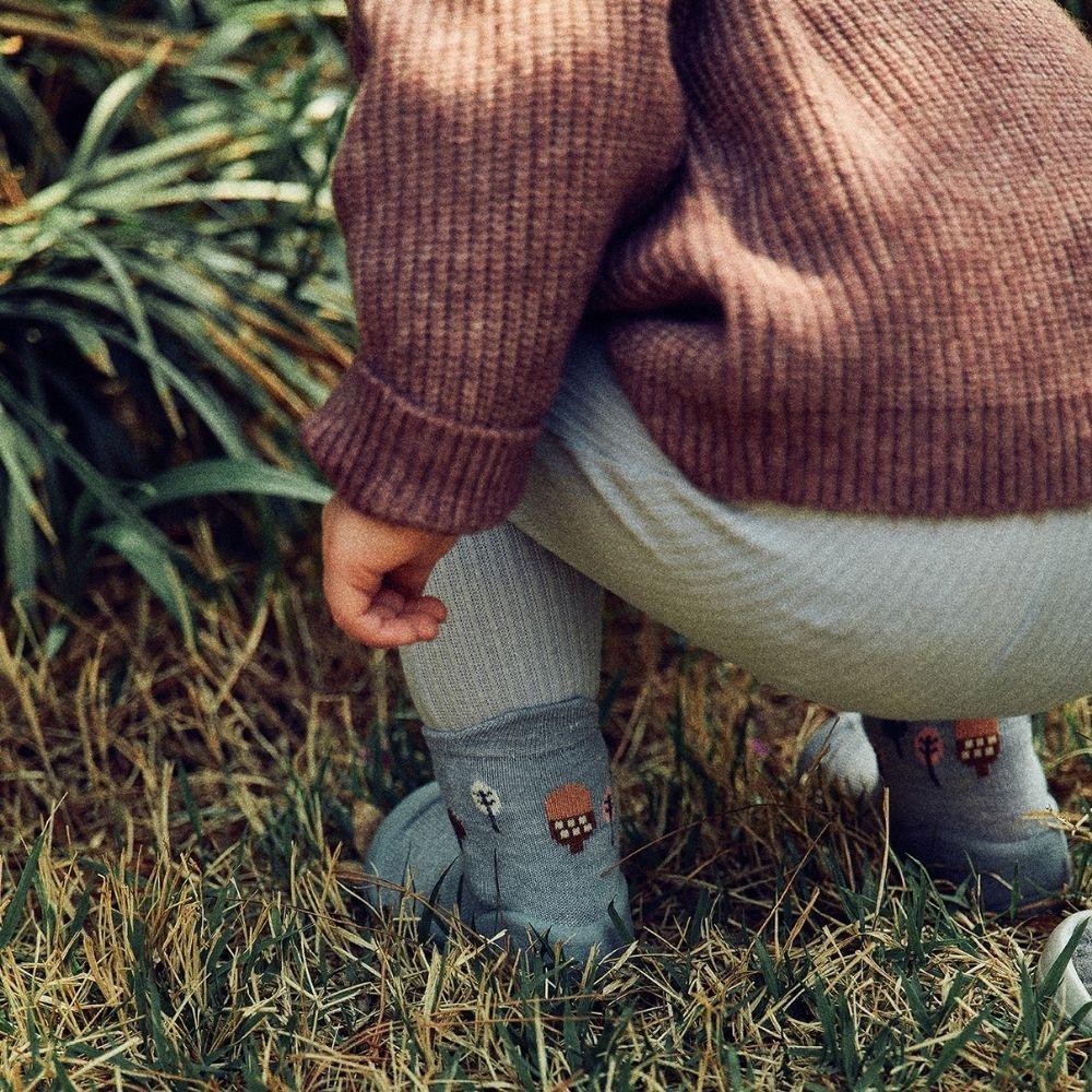 Criança agachada em gramado, usando meias Attipas Woodland Blue Squirrel com estampa de esquilos.